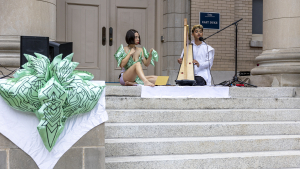 Two performers sitting on the steps of a building  one playing a harp