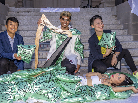 4 people posing with a small harp and green and black pillows on steps of a building