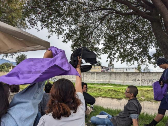 Women wave purple and black fabric in front of prison wall
