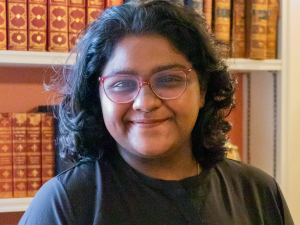 Headshot of Indian woman in Black T-shirt in front of book case
