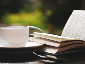 Open book, white cup and saucer with spoon outside