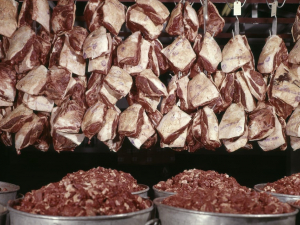 cuts of red meat hanging over buckets of ground meat