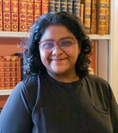 Headshot of Indian woman in Black T-shirt in front of book case